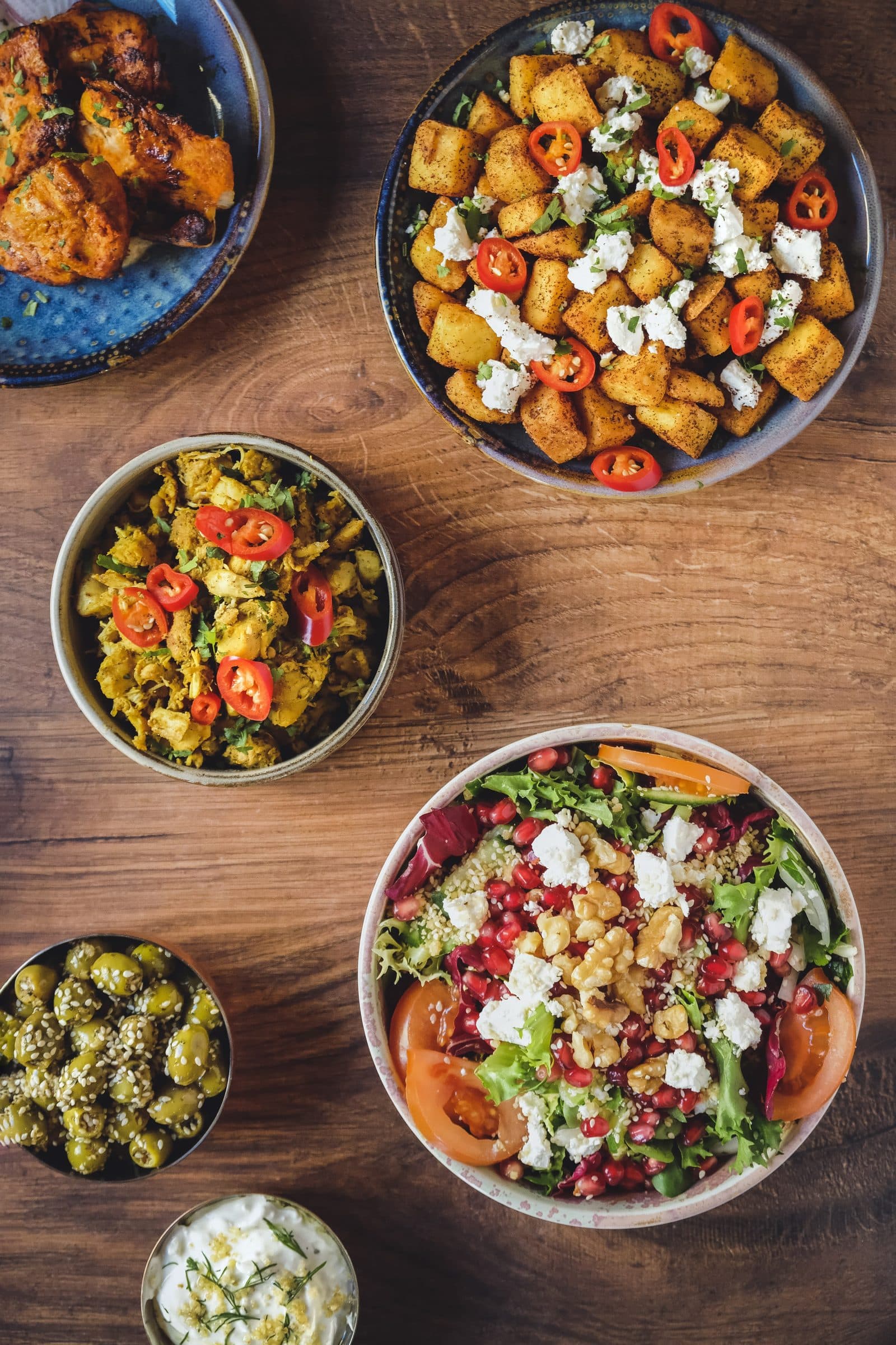 Mazzeh bowls on wood — spiced potatoes with feta and chilli, saffron chicken, pomegranate salad and olives