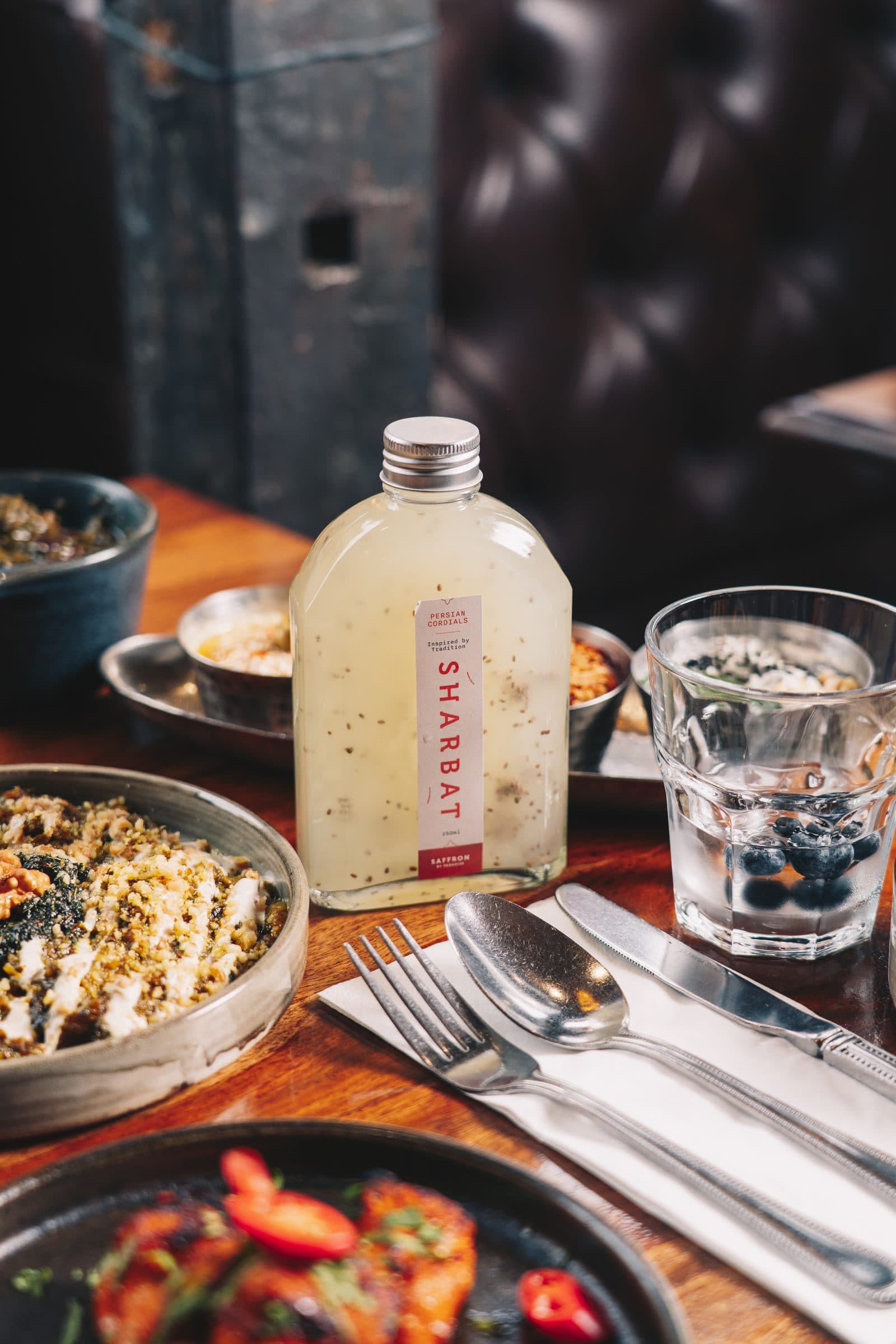 A bottle of house sharbat, iced water and mazzeh plates on a candlelit table